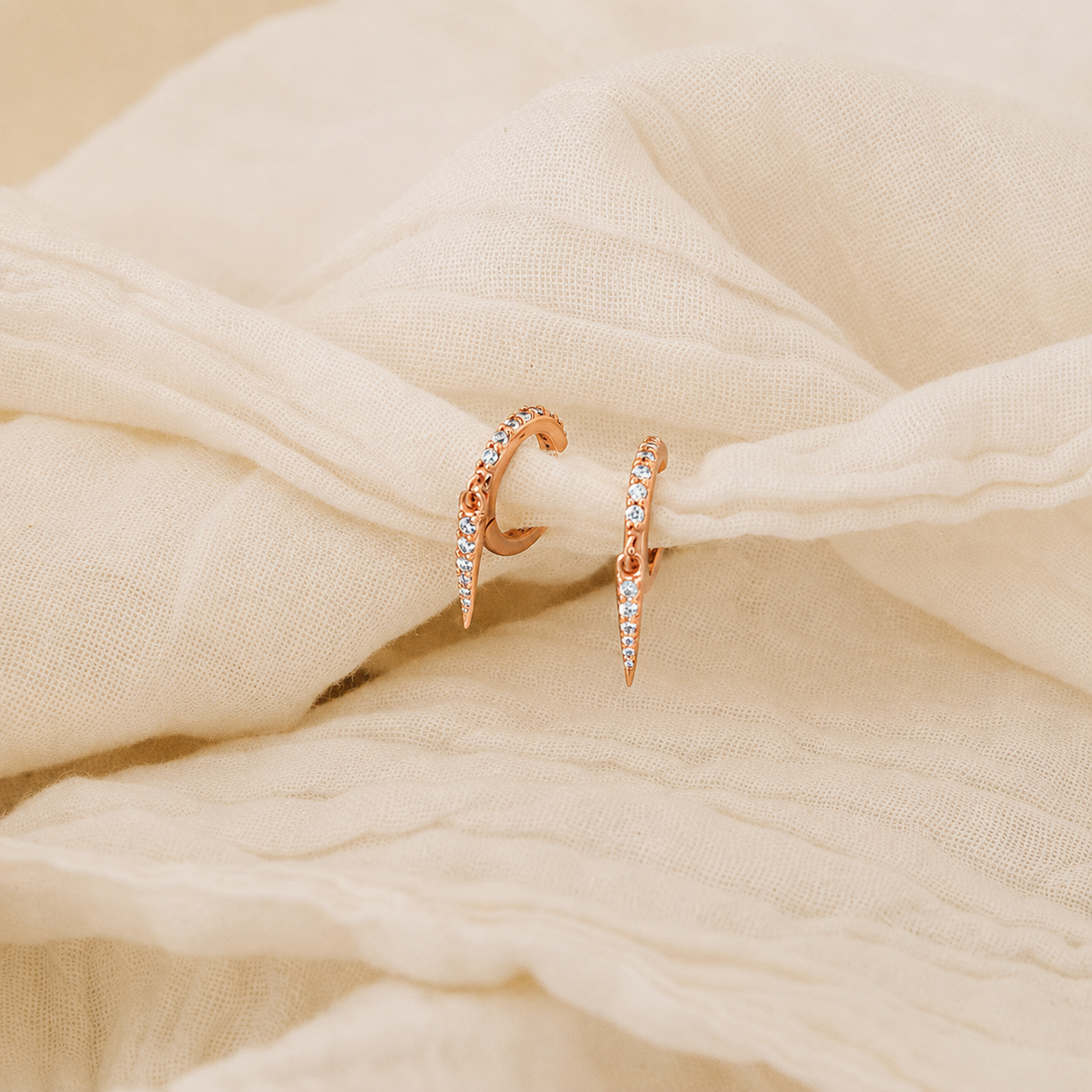 Rose gold hoop earrings with small diamonds on a beige fabric background